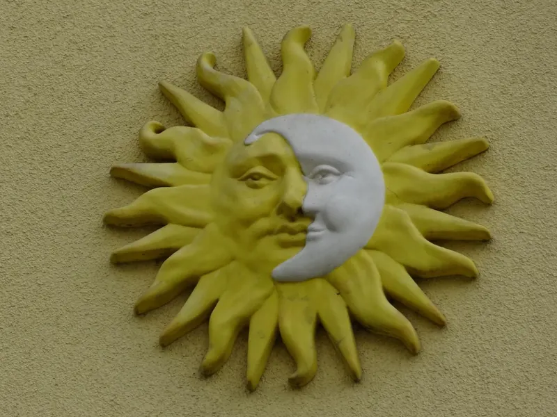 Keramické slunce s měsícem na žluté fasádě penzionu